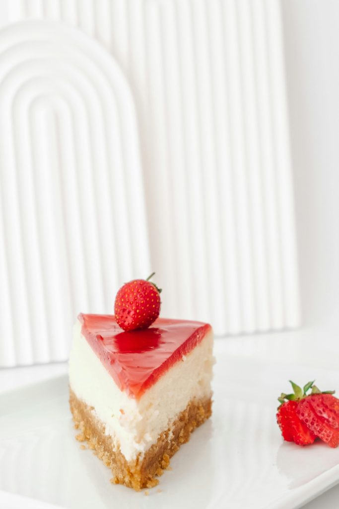Delicious strawberry cheesecake slice with a graham crust on a white plate.